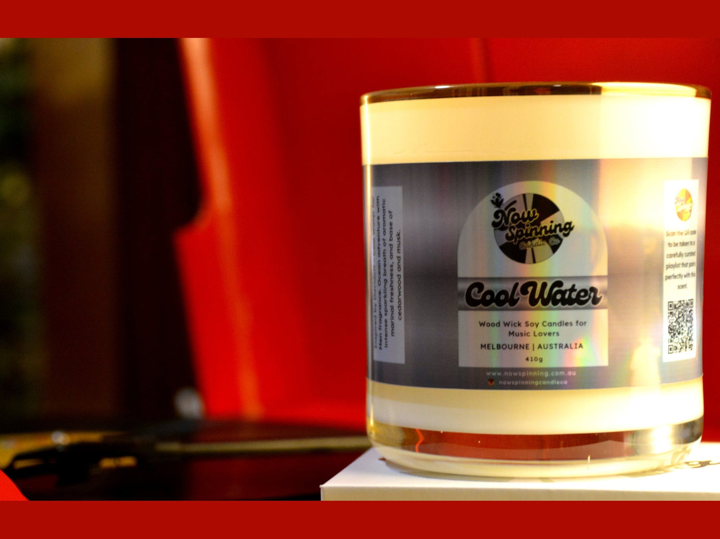 Candle labeled 'Cool Water' byon a stand with a blurred red background