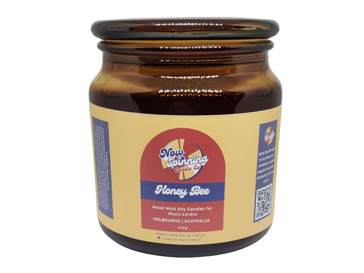 A jar of 'Honey Bee' wood wick candle for Melbourne Australia. The label has a yellow and red design with a honeycomb pattern and a QR code.