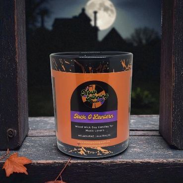 Candle with 'Now Spinning' label in front of a moonlit house silhouette