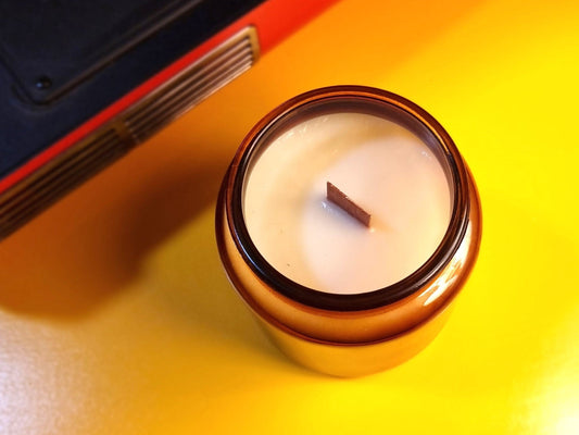 Candle in an amber jar  on a yellow surface with a red and black object in the background
