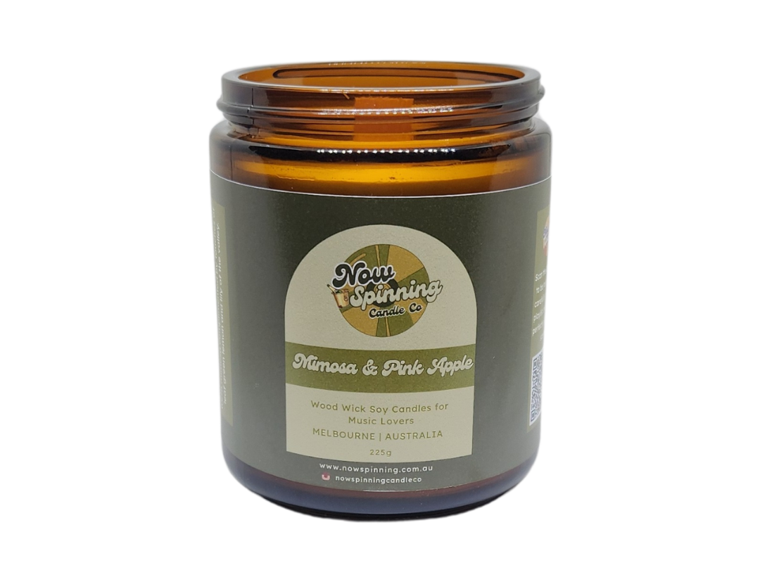 A brown amber glass jar candle with a black screw top lid, labeled 'Mimosa & Pink Apple'.