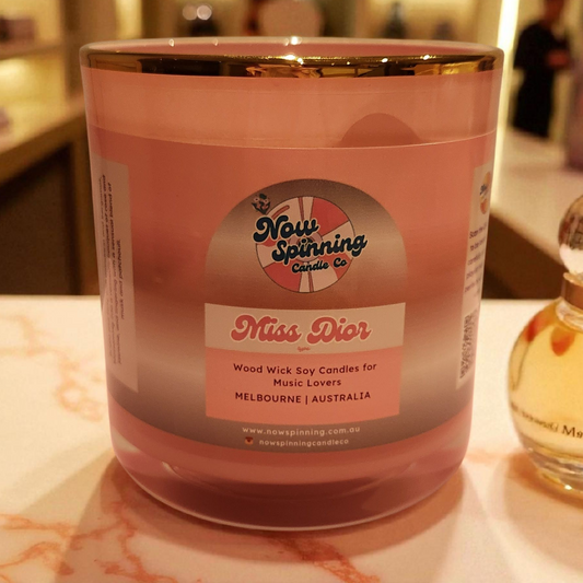 Pink candle labeled 'Miss Dior' with a bottle of perfume in the background