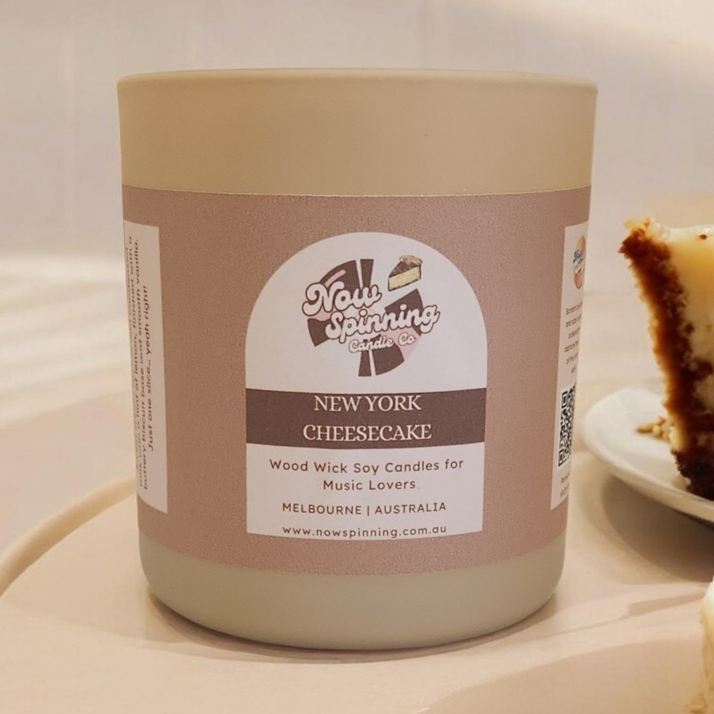 Candle labeled 'New York Cheesecake' from Now Spinning on a white surface with a blurred background