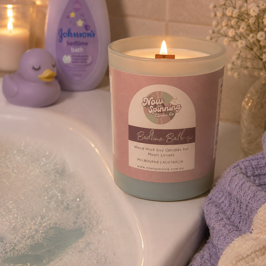Candle with a label in a bathroom setting with a bathtub, towel, and baby products.