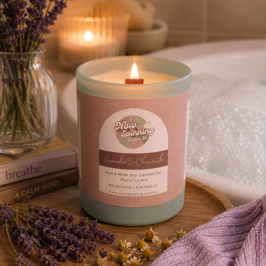 Candle with a label on a wooden tray surrounded by lavender and books, with a blurred background.