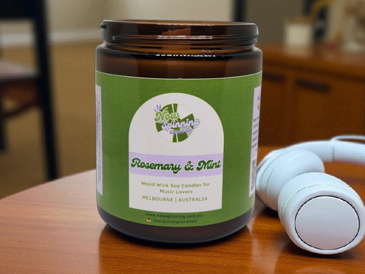 Candle jar with a green label on a wooden surface, with a white candle in the background.
