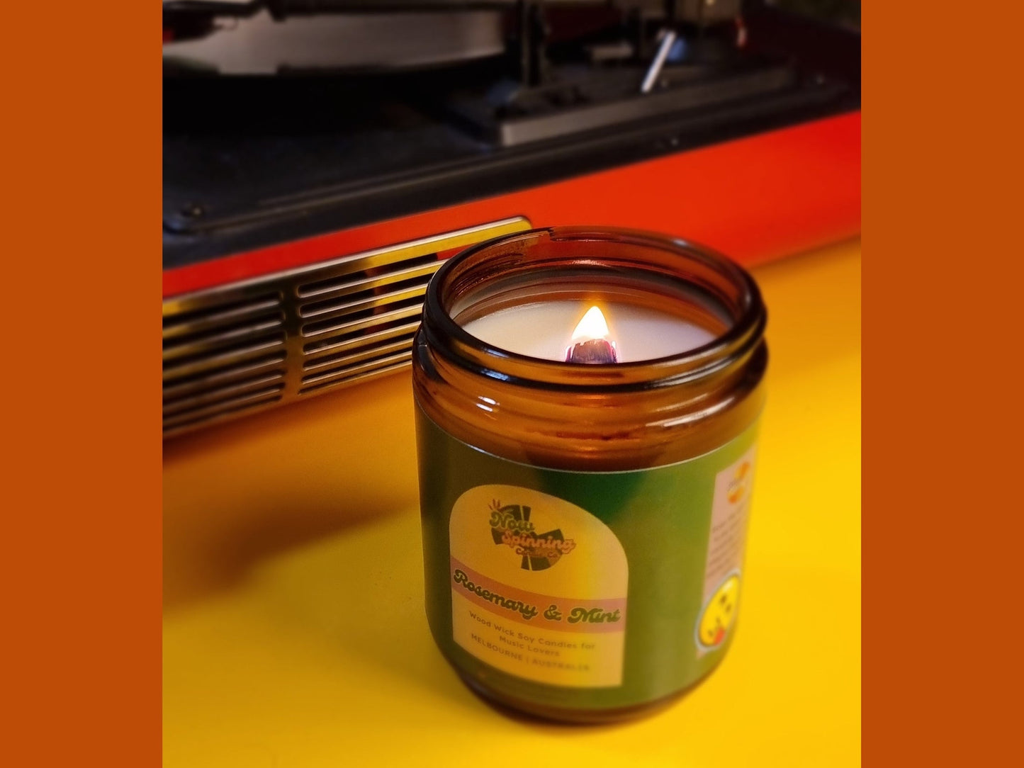 Candle in a jar with a label in front of a record player on a yellow surface