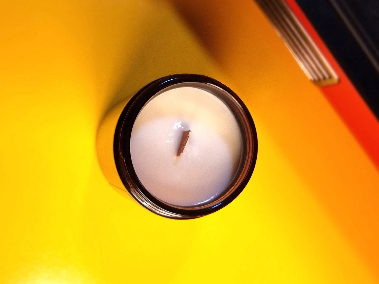 Wood Wick Candle in an amber glass jar on a yellow surface