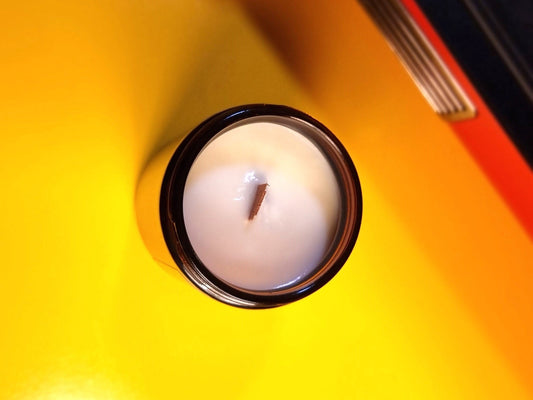 Wood Wick Candle in an amber glass jar on a yellow surface