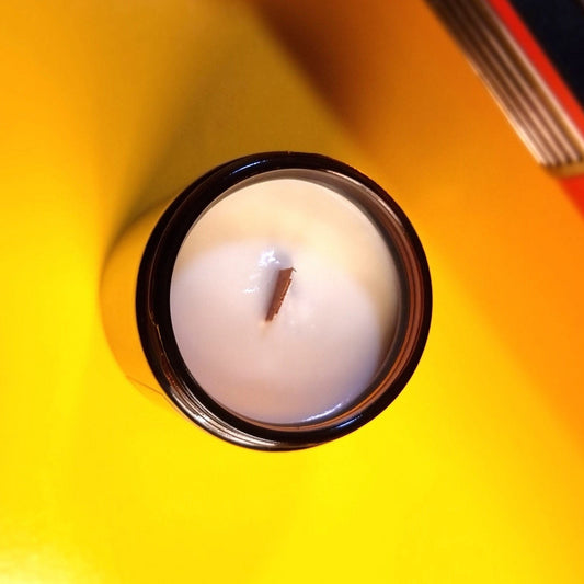 Wood Wick Candle in an amber glass jar on a yellow surface