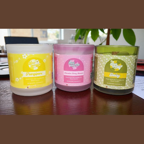 Three scented candles with colorful labels on a reflective surface.