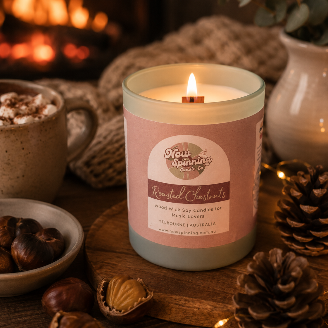 Roasted Chestnuts candle from Now Spinning Candle Company displayed beside roasted chestnuts, hot chocolate and a crackling fireplace. This wood wick soy candle combines warm winter fragrance with a curated playlist, creating the perfect soundtrack for cosy evenings at home.