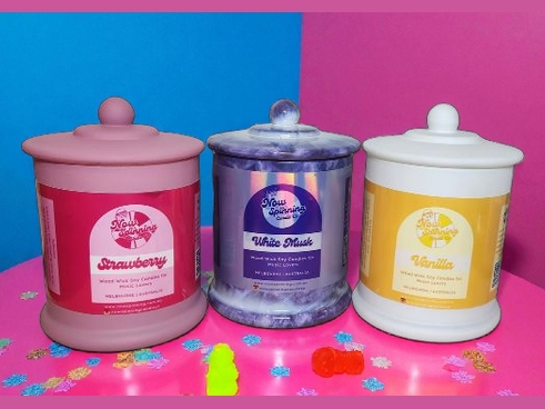 Three scented candles with colorful labels on a pink and blue background