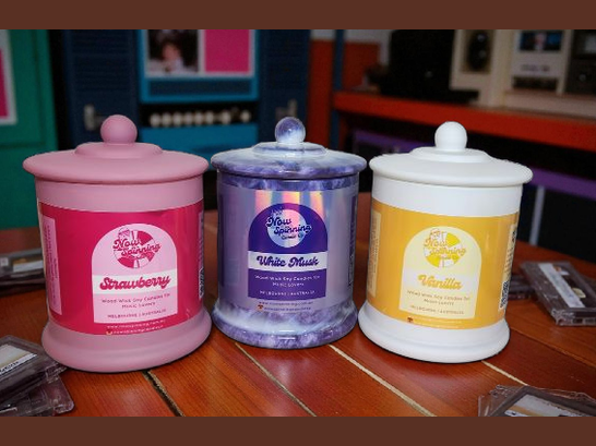Three scented candles with labels on a wooden surface.