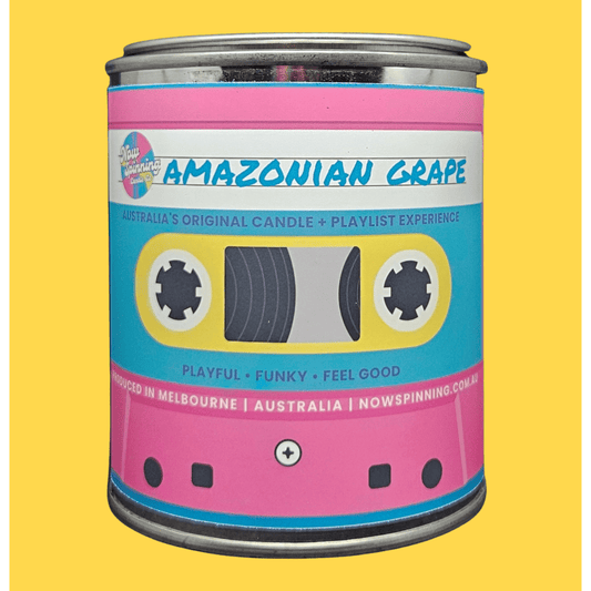 A novelty candle tin styled like a retro cassette tape, featuring a pink and light blue label with the text 'AMAZONIAN GRAPE' and 'Australia's Original Candle + Playlist Experience' on a solid yellow background.