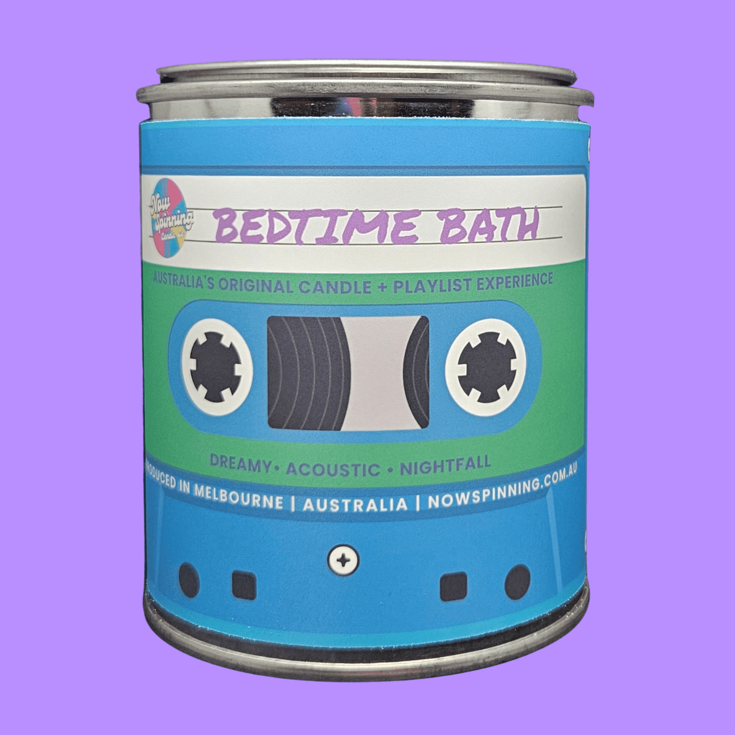 A cylindrical metal tin candle labeled 'BEDTIME BATH' with a cassette tape graphic on the front, shown against a solid lavender background.