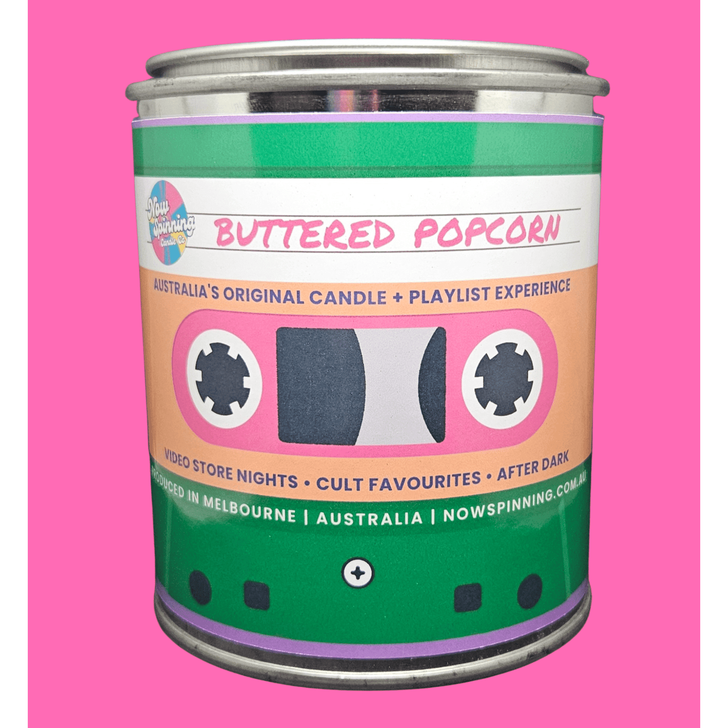 A novelty tin candle shaped like a cassette tape, labeled 'Buttered Popcorn' by Nowspinning, set against a solid pink background.
