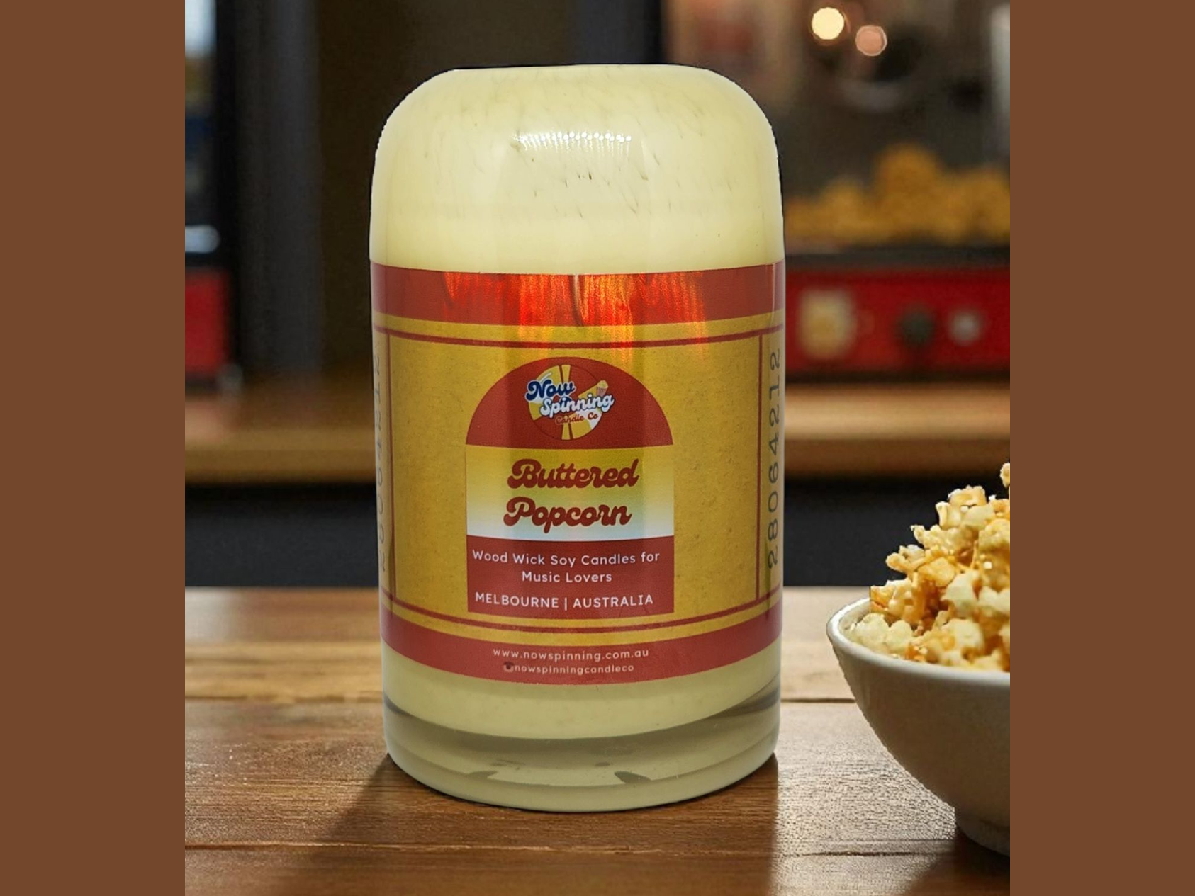 Buttered Popcorn candle in a glass jar with a label on a wooden surface.