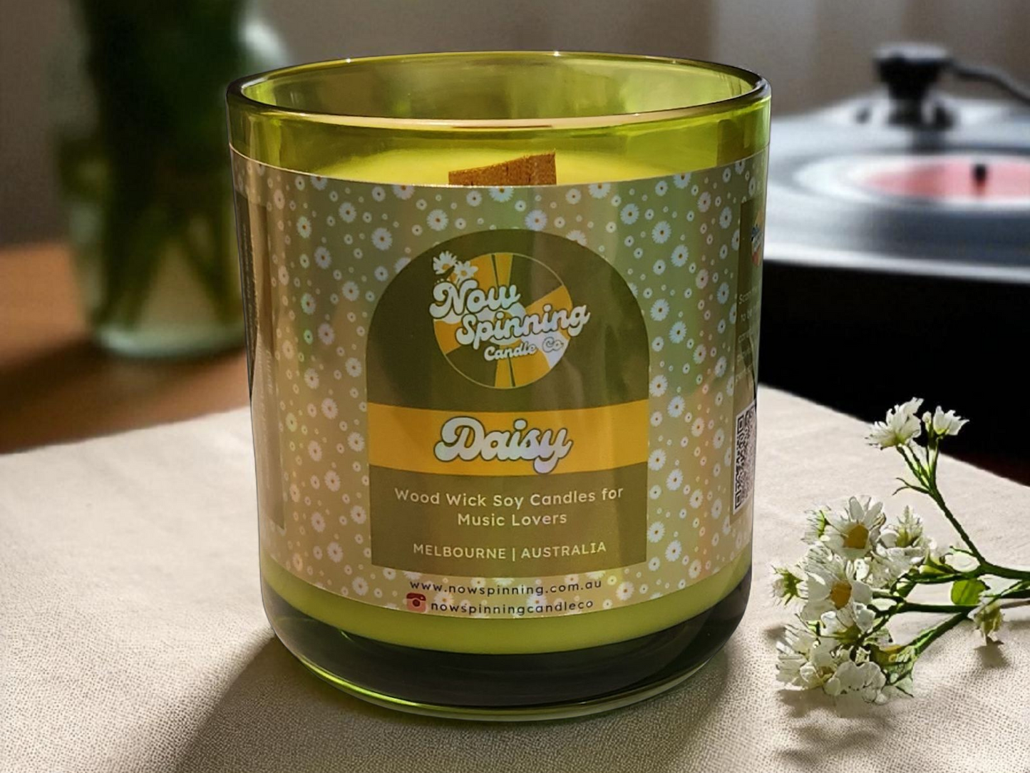 Green candle with a label on a table with flowers in the background