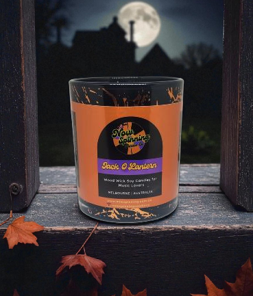 Candle with 'Now Spinning' label in front of a moonlit house silhouette