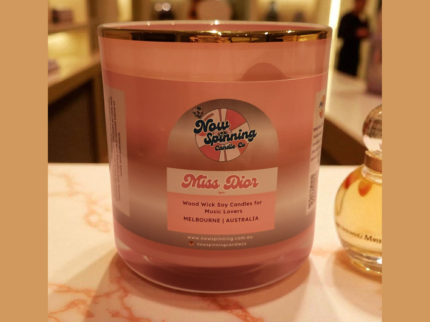 Pink candle labeled 'Miss Dior' with a bottle of perfume in the background
