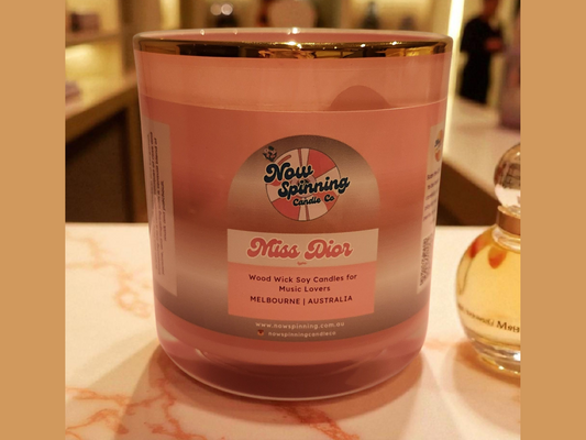 Pink candle labeled 'Miss Dior' with a bottle of perfume in the background