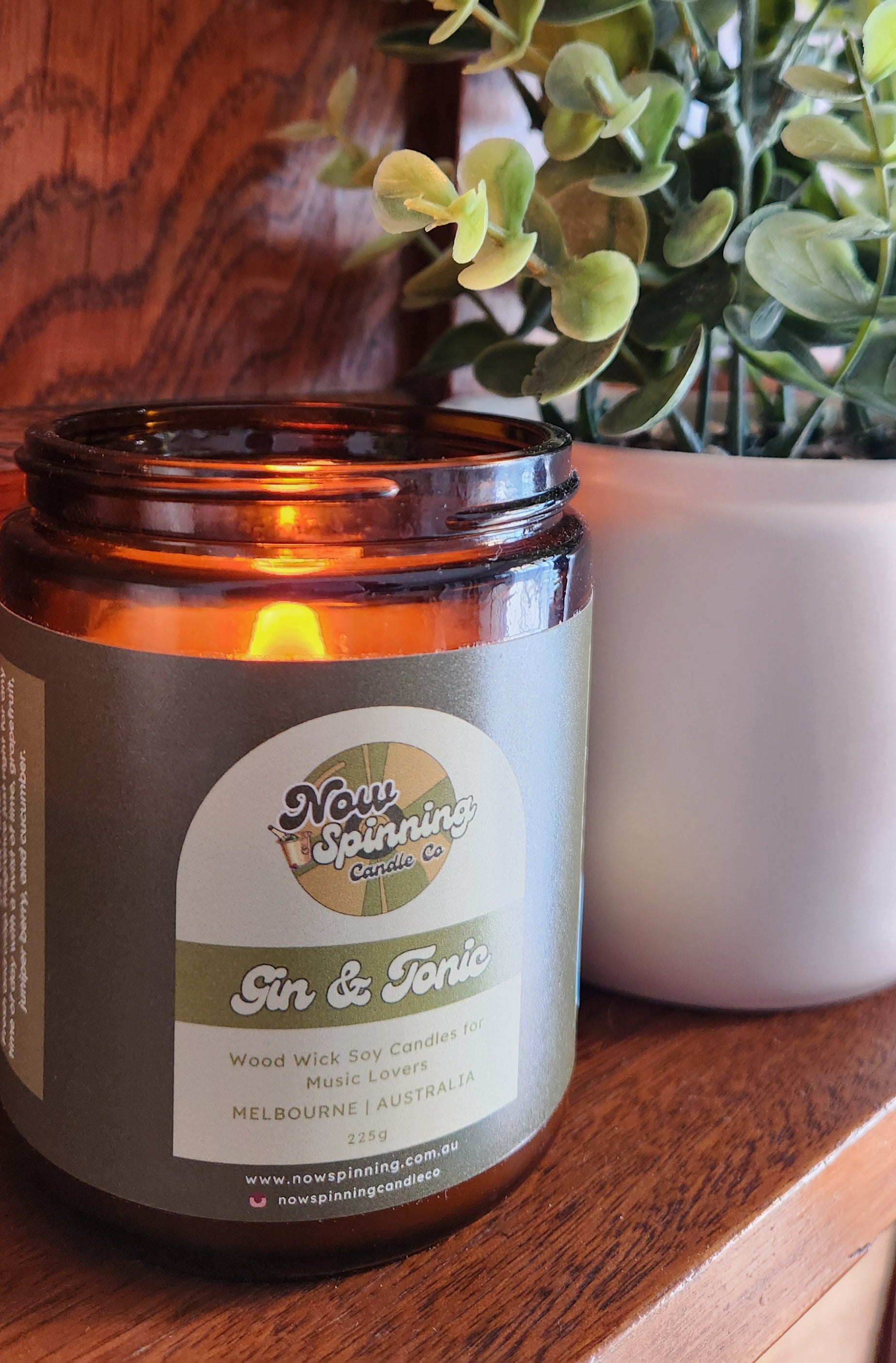 Candle jar labeled 'Gin & Tonic' with a plant in the background on a wooden surface