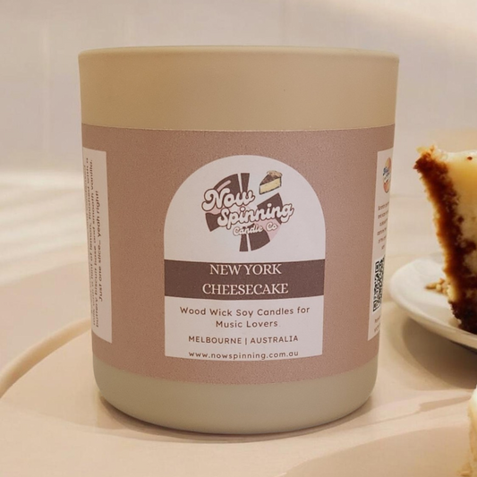 Candle labeled 'New York Cheesecake' from Now Spinning on a white surface with a blurred background