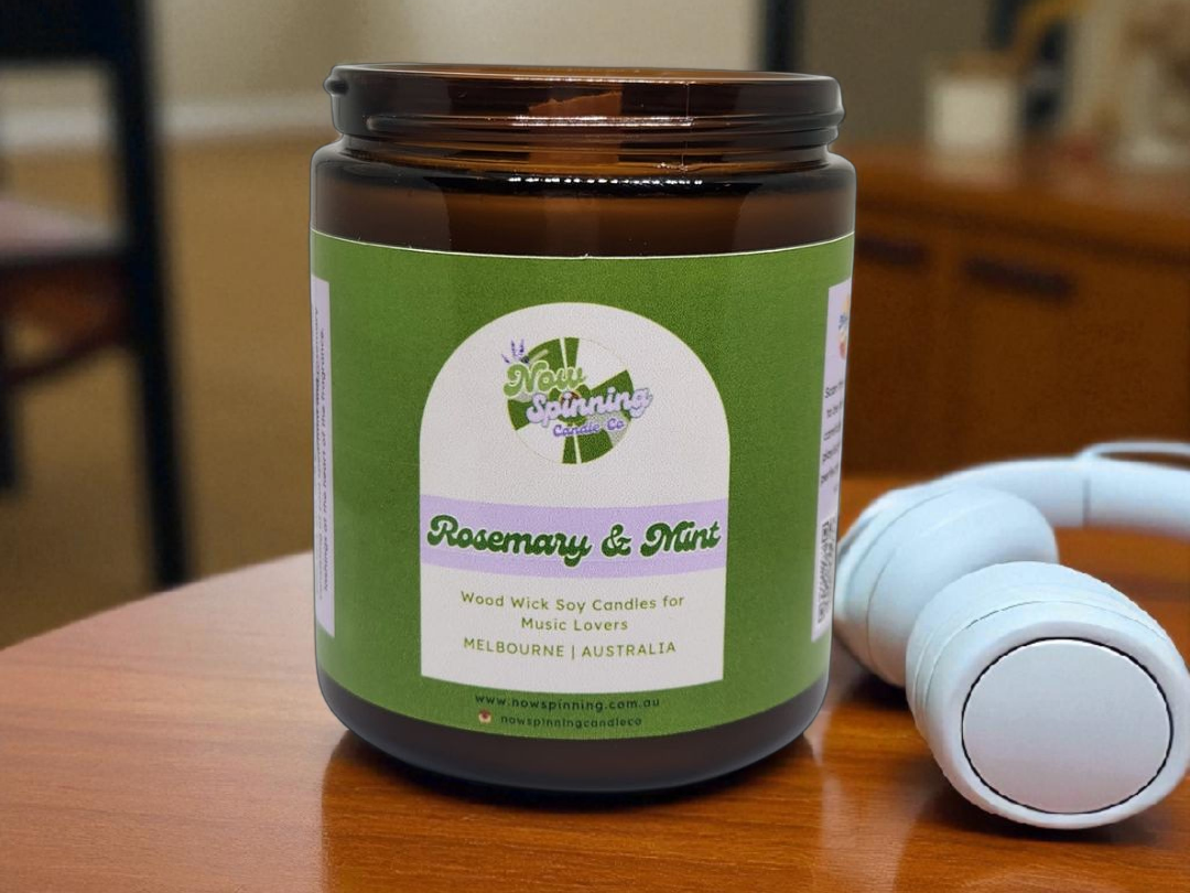 Candle jar with a green label on a wooden surface, with a white candle in the background.