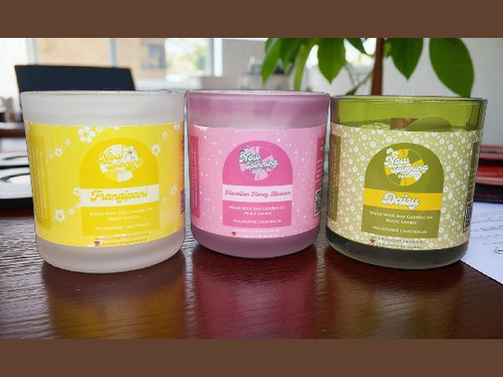 Three scented candles with colorful labels on a reflective surface.