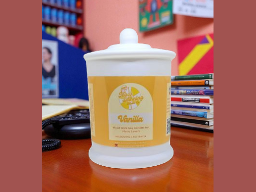 Vanilla-scented candle jar on a desk with books and a computer mouse in the background