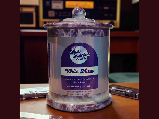 White Musk candle with a purple label on a wooden surface