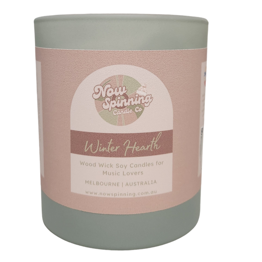 Winter Hearth wood wick soy candle by Now Spinning Candle Company featuring smoky firewood, amber and pine notes. Styled in a cosy winter setting inspired by crackling fireplaces, warm blankets and relaxing evenings at home.
